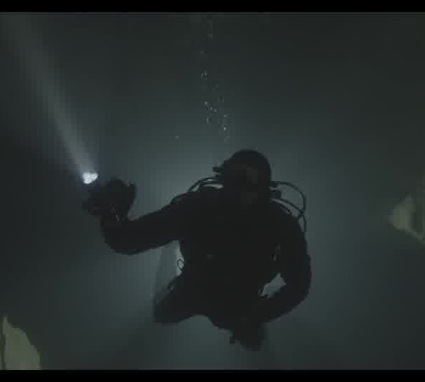 Diver_with_a_flashlight_swimming_in_a_dark_underwater_cave_1609300K